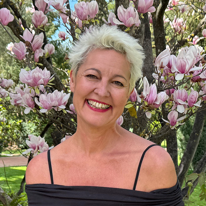 Myrto Mangrioti smiling in front of blooming magnolia tree, representing growth and confidence in sharing your message