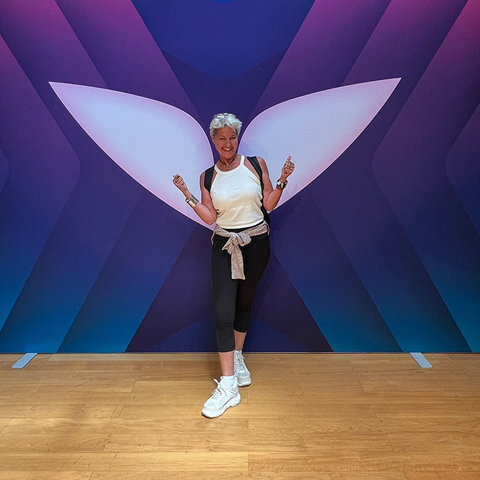 Myrto Mangrioti posing playfully in front of large wing backdrop, symbolising freedom and transformation after speaking your truth